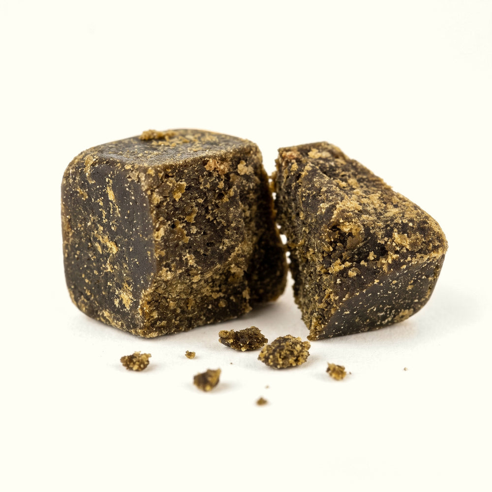 Nine Realms CLASSIC Dry Sift Hash in Nahaufnahme: dunkler, gepresster Block, in zwei Hälften gebrochen, mit Krümeln auf cremefarbenem Hintergrund